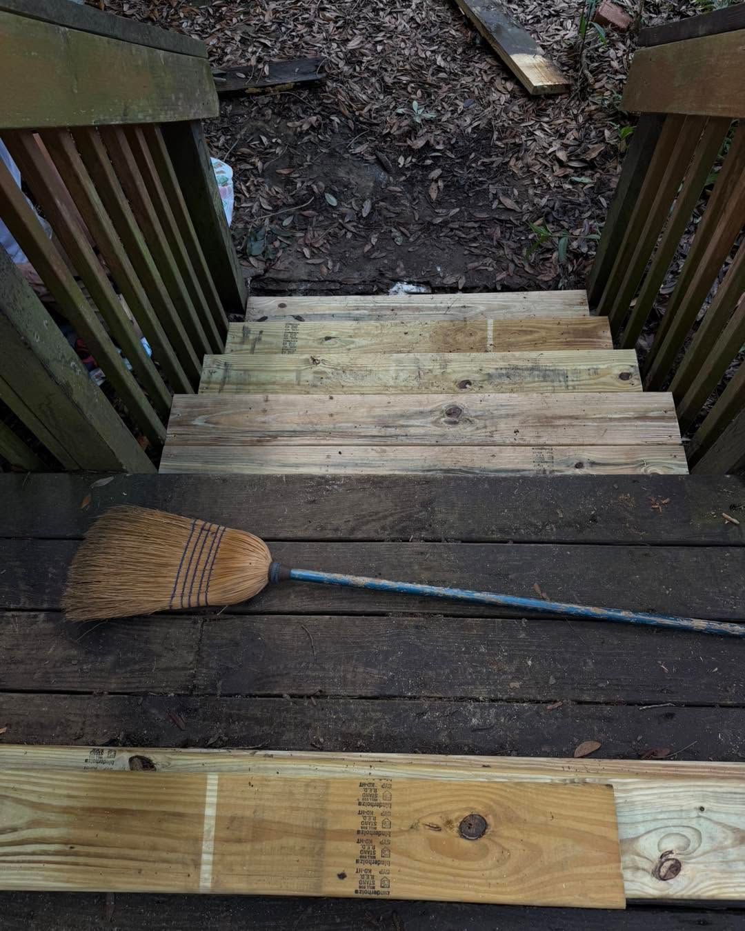 Broom and long-handled tool on wooden steps leading to a muddy yard.