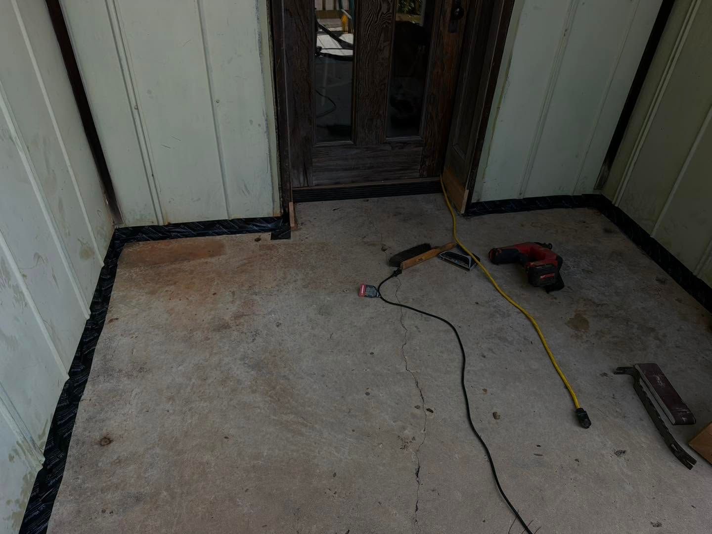 Small room with unfinished floor, doorway, and scattered tools including a cord, drill, and tape measure.