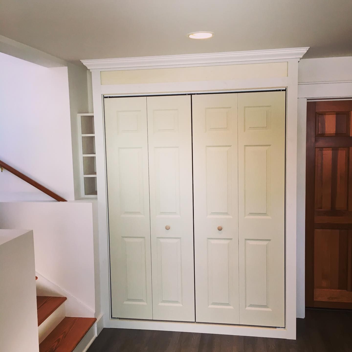Built-in white double closet doors in a hallway beside stairs and wood trim.