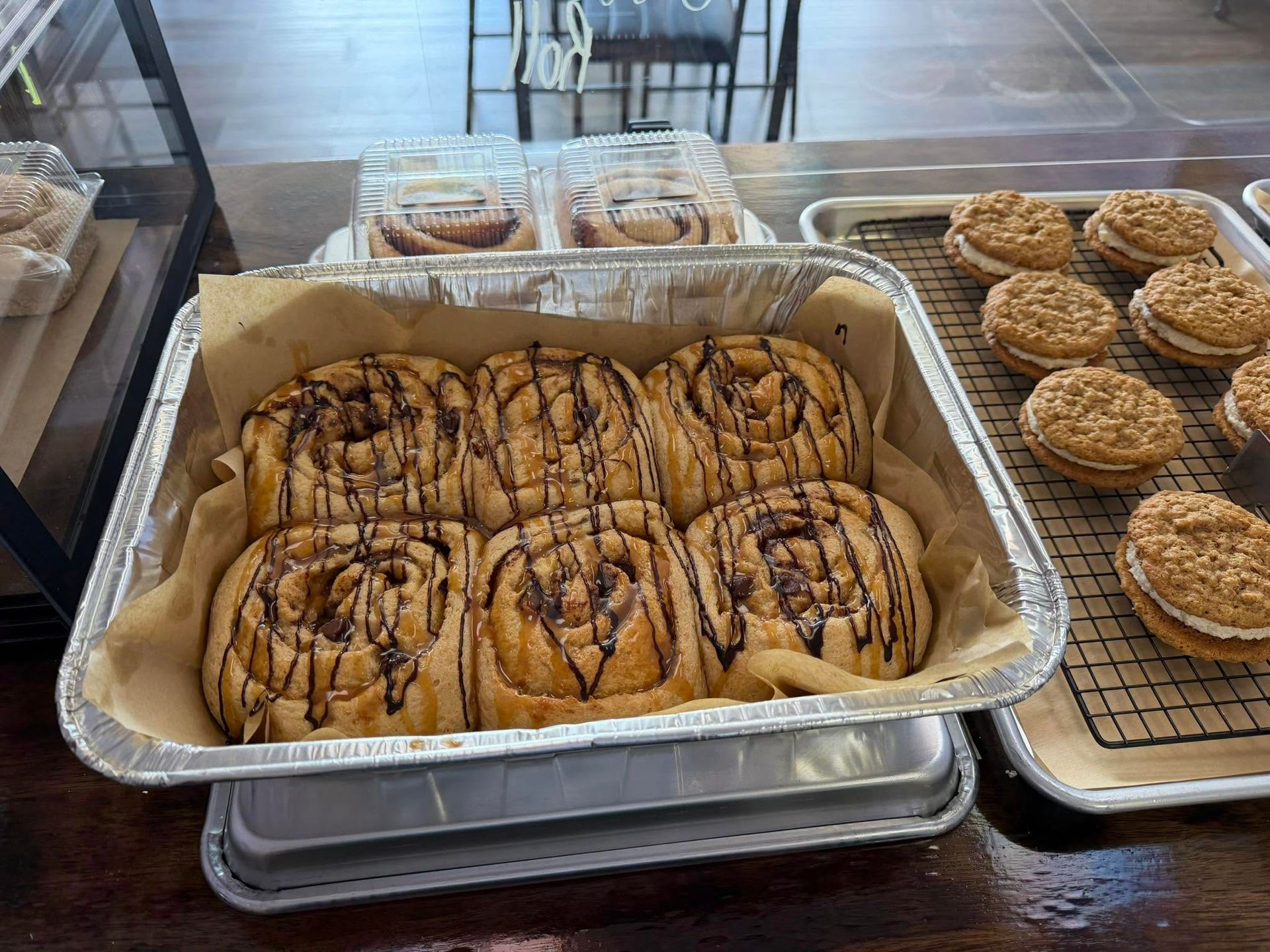 Tray of iced cinnamon rolls in a bakery display case beside round pies or pastries