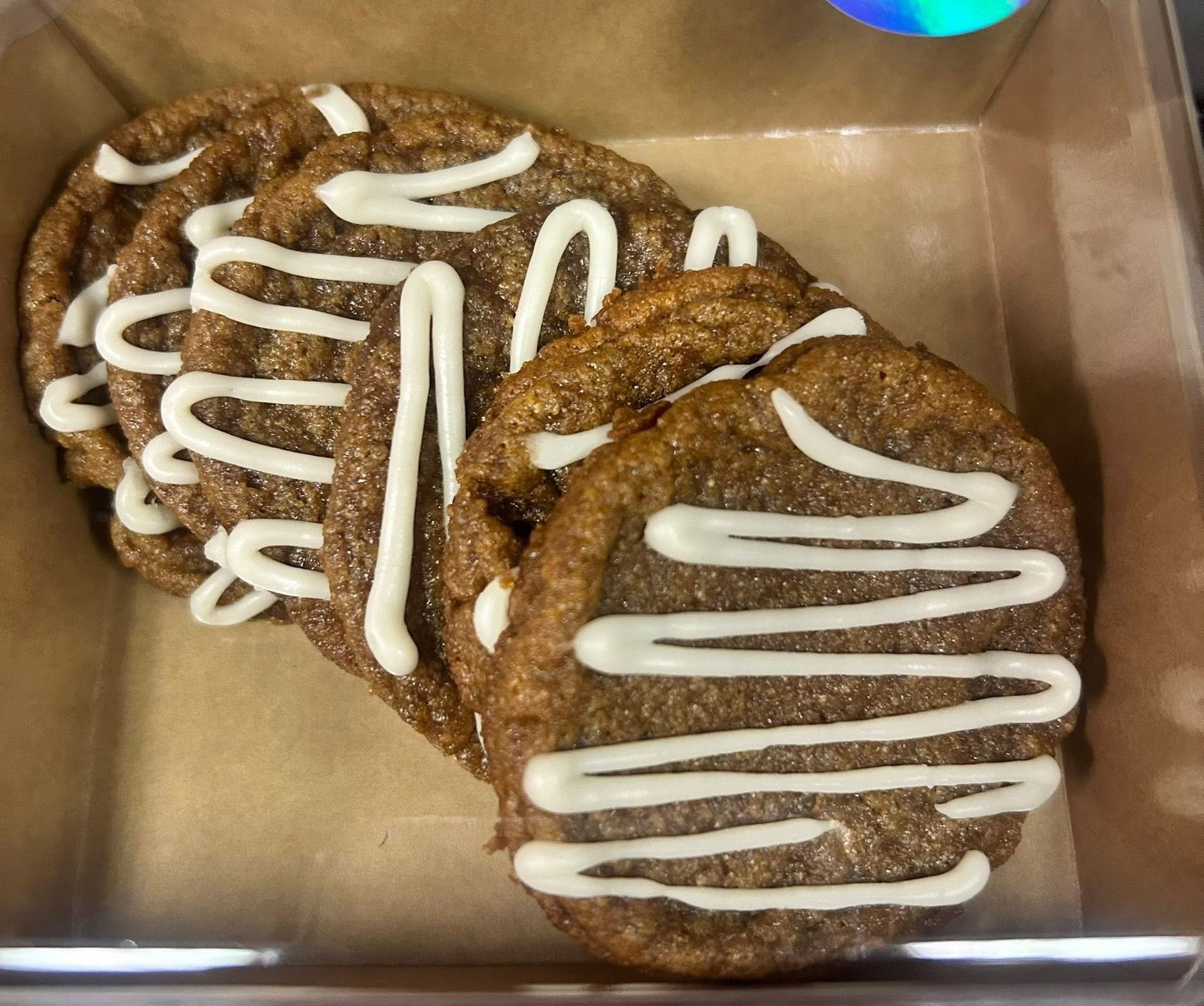 Two oatmeal cookies with white icing in a clear plastic container