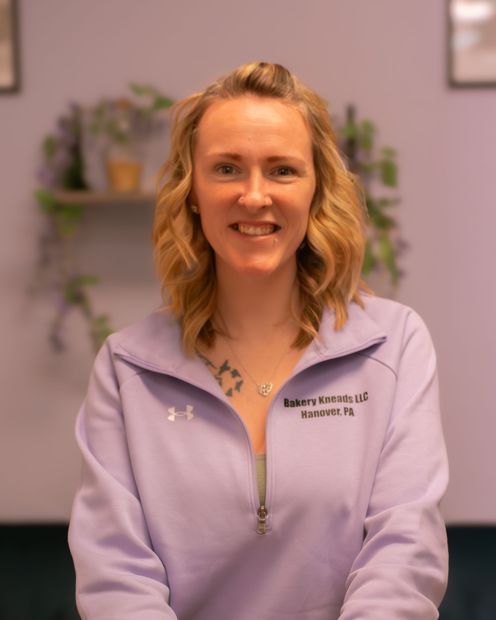 Woman in a lavender zip-up sweatshirt smiling in a softly lit indoor setting.