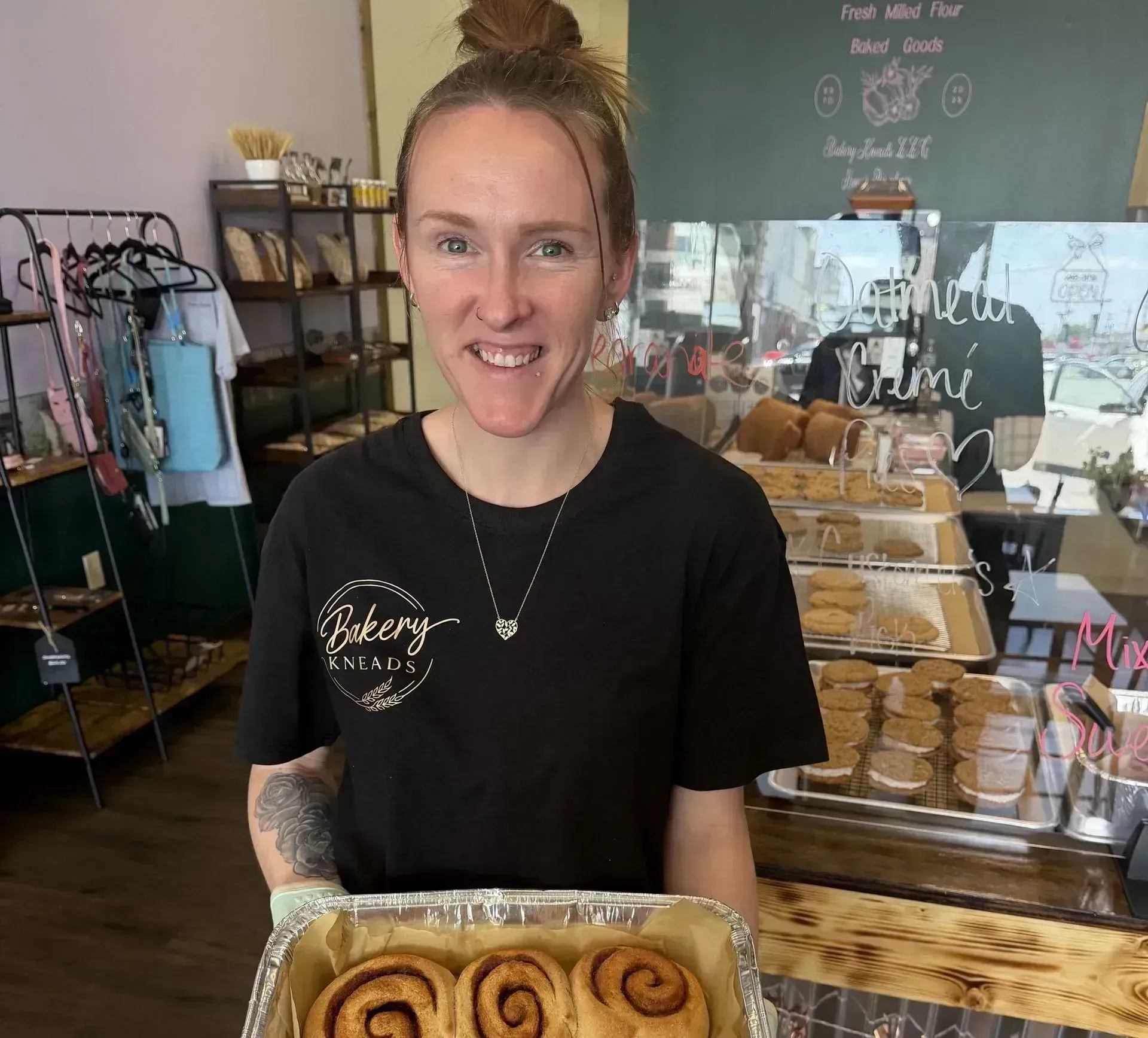 Bakery worker smiling and holding a tray of cinnamon rolls in a shop