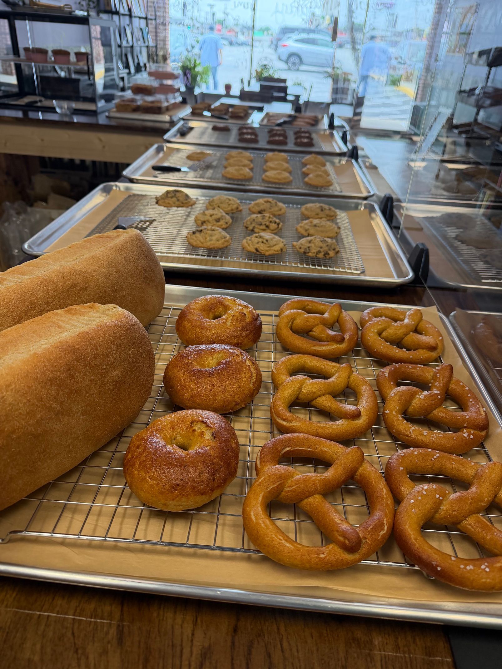 Bakery display with assorted pretzels, rolls, and pastries on trays behind a glass counter