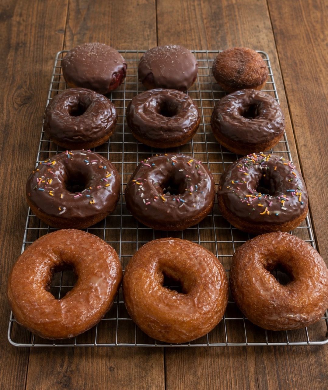 Assorted glazed donuts on cooling racks, including chocolate and plain varieties on a wooden table.