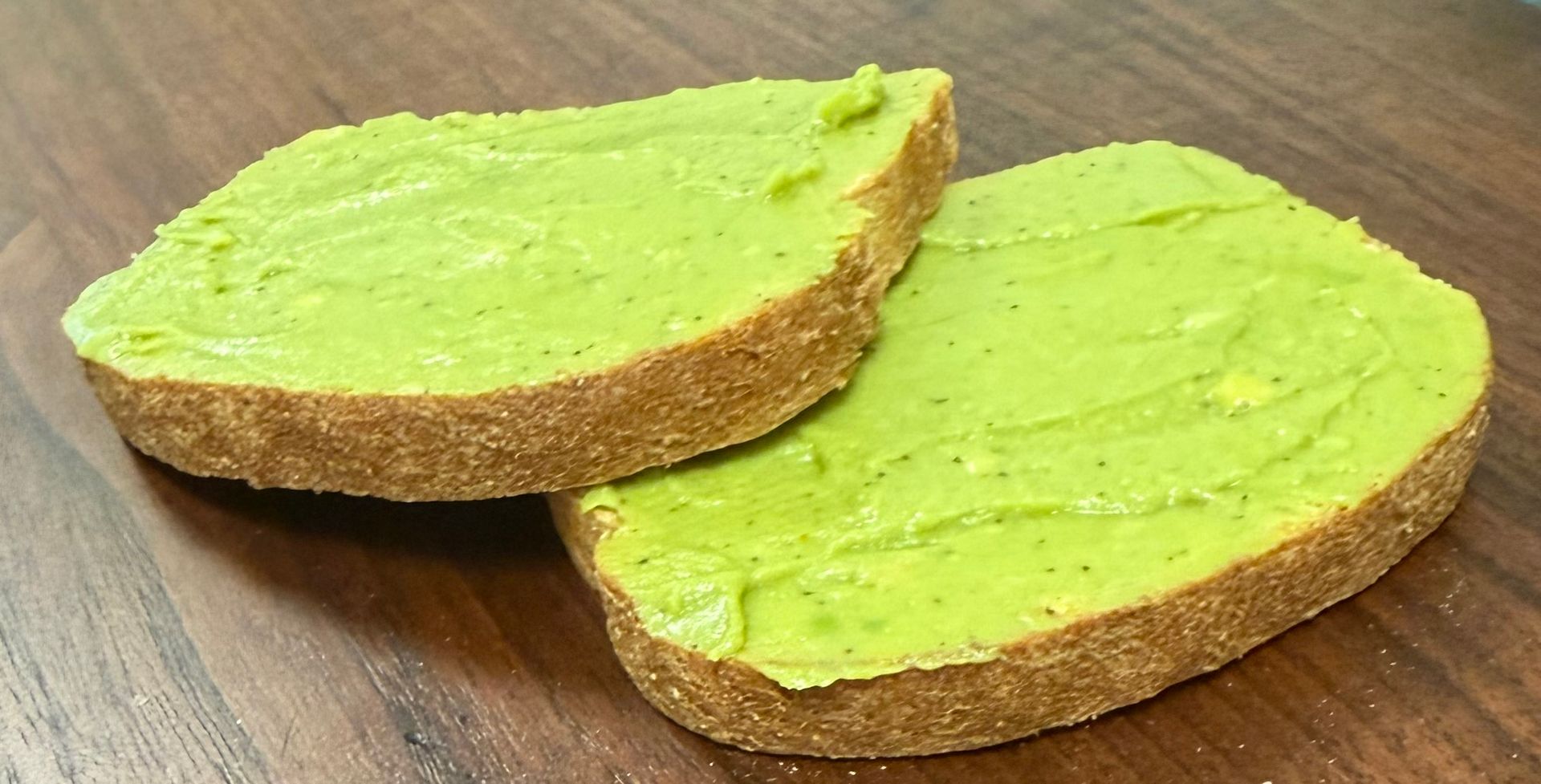 Two slices of bread topped with green spread on a wooden table