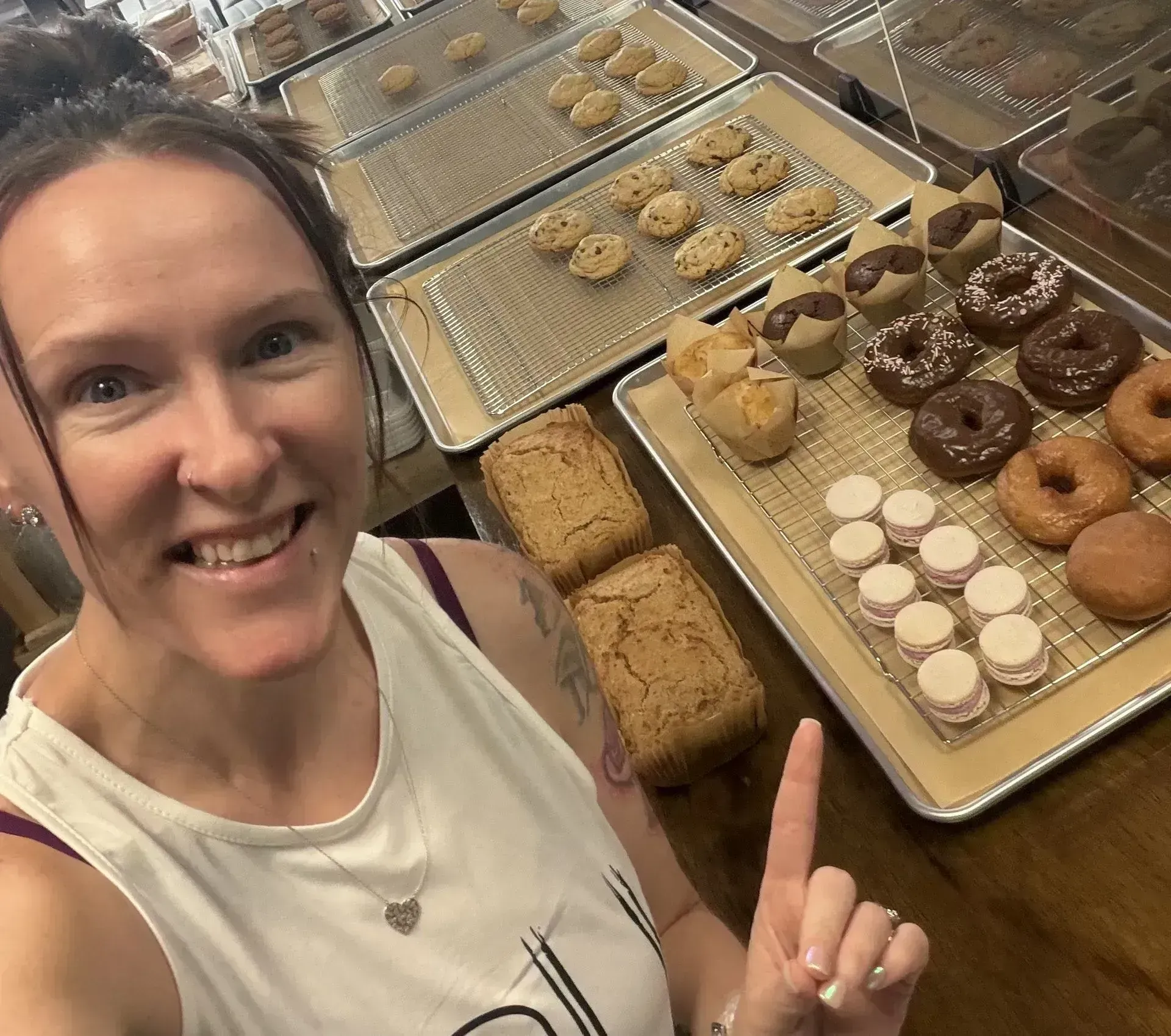 Smiling woman points at trays of assorted donuts on a bakery counter