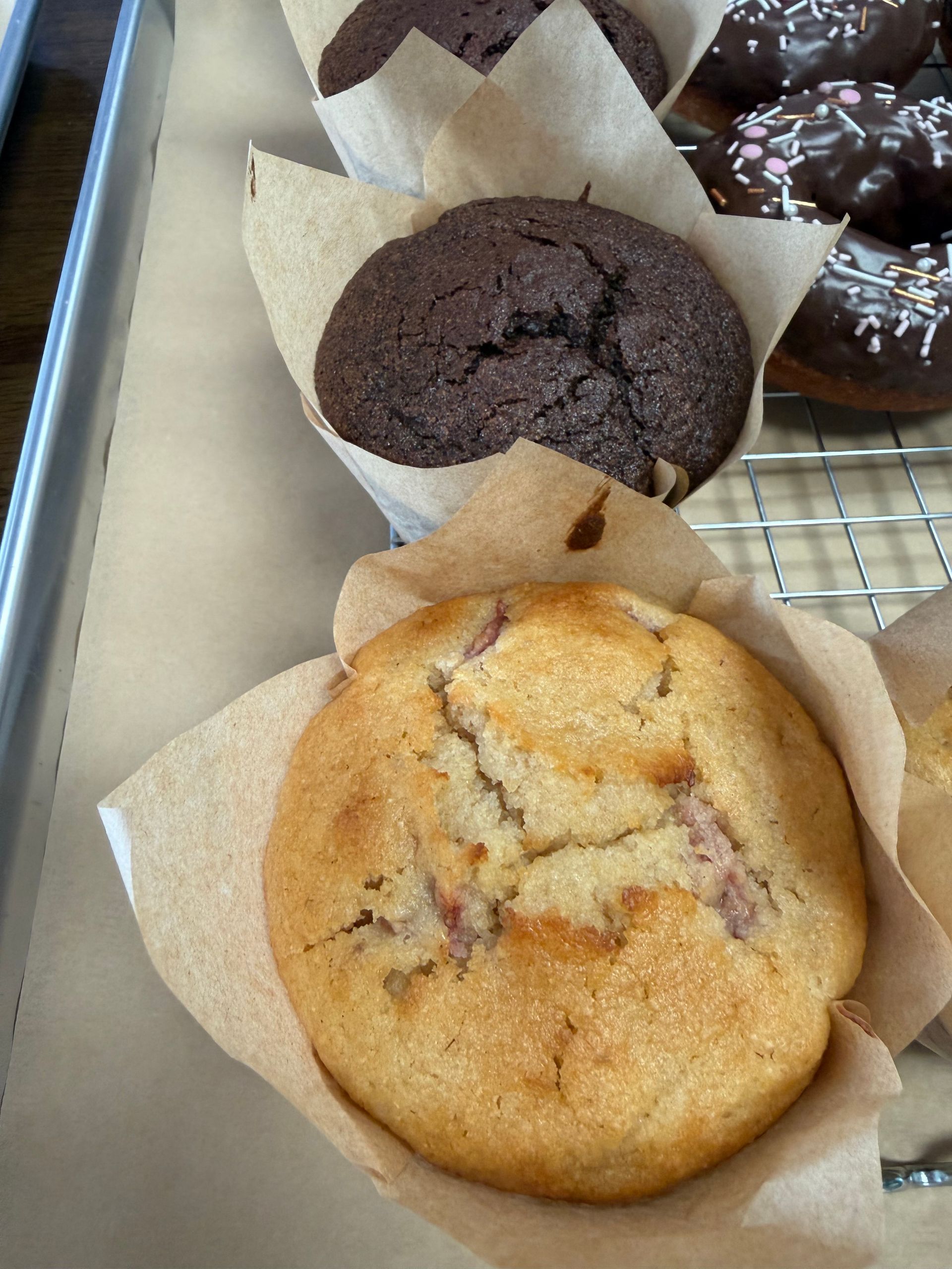 Assorted muffins in a bakery box, including chocolate and fruit-topped varieties on parchment liners