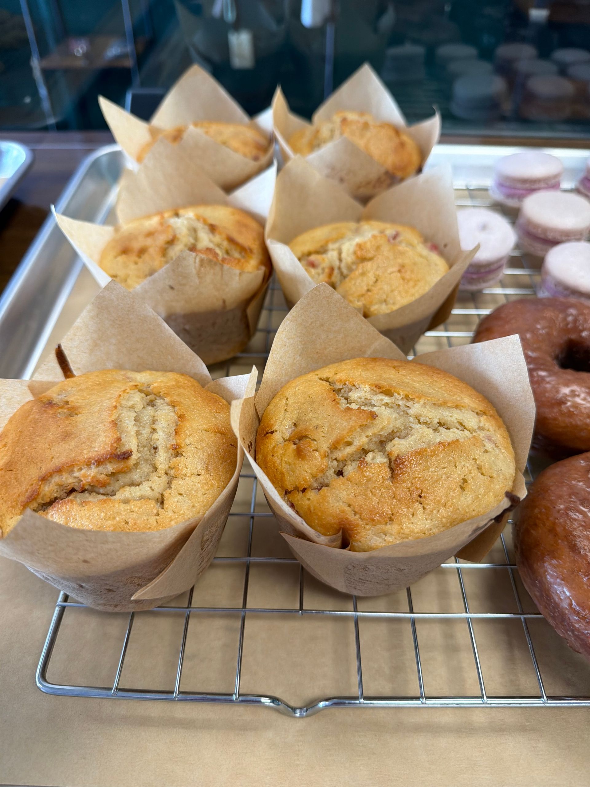 Freshly baked muffins in paper liners cooling on a wire rack, with several more trays in the background.
