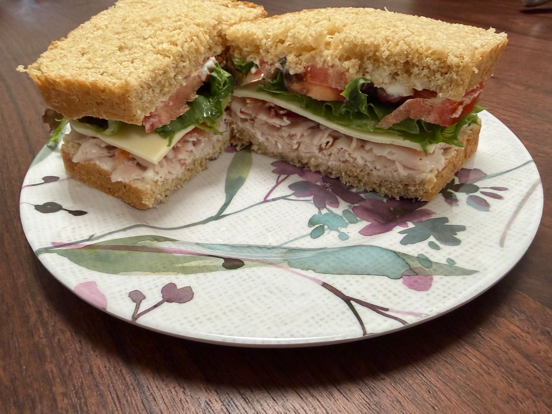 Cut sandwich with lettuce, tomato, and cheese on a floral plate on a wooden table