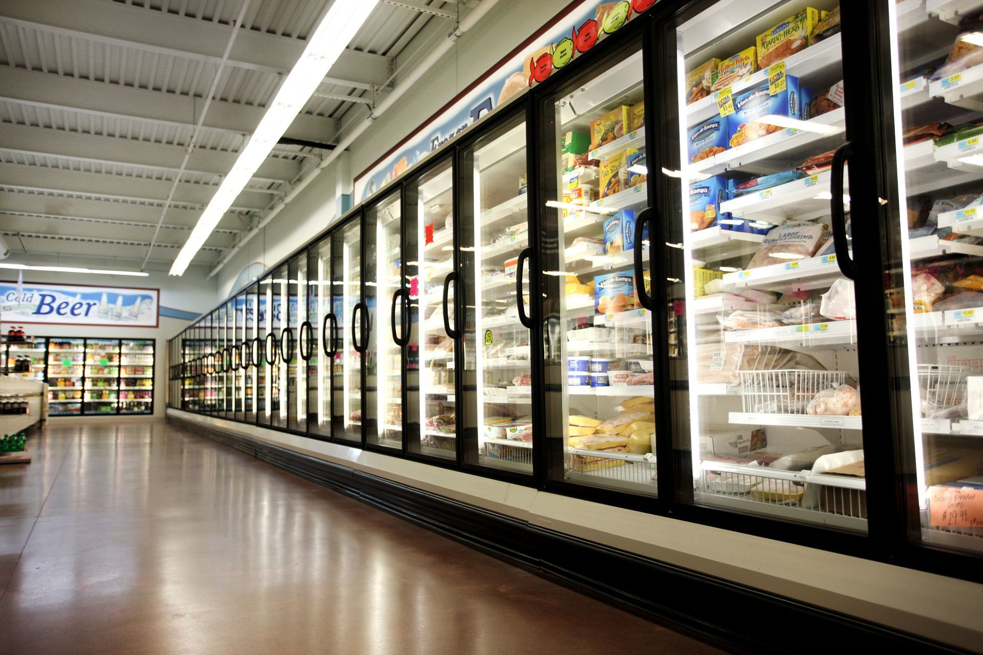 Empty grocery aisle with glass-door refrigerators filled with products.