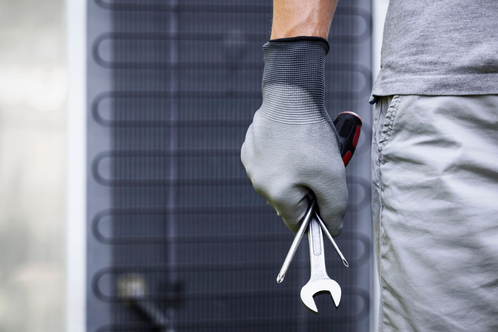 Person wearing gloves holding a wrench and screwdriver near equipment.