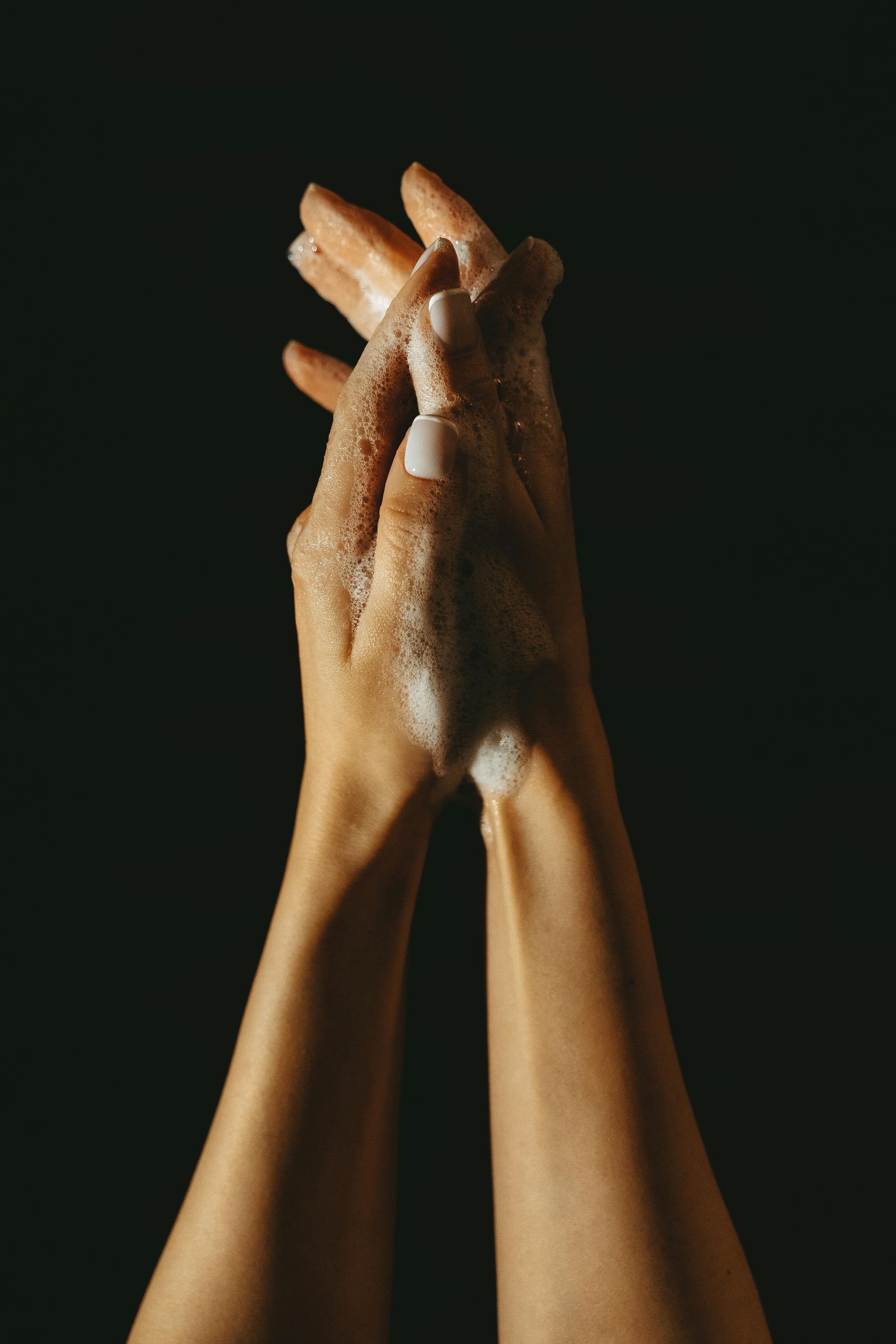 Hands clasped and covered in soap against a black background.