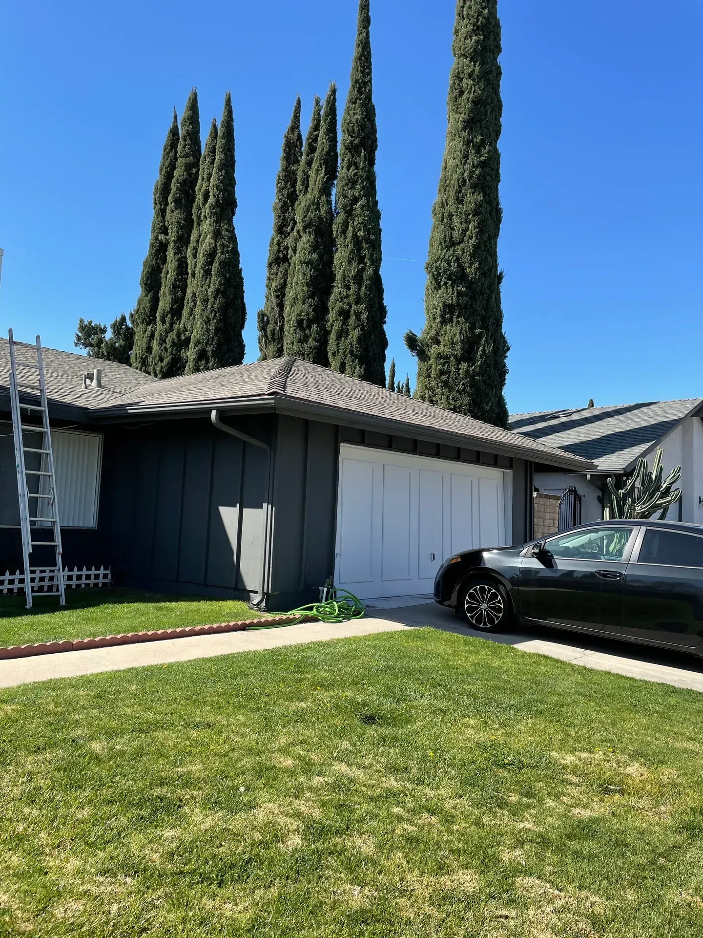 A black car is parked in front of a house with trees in the background.