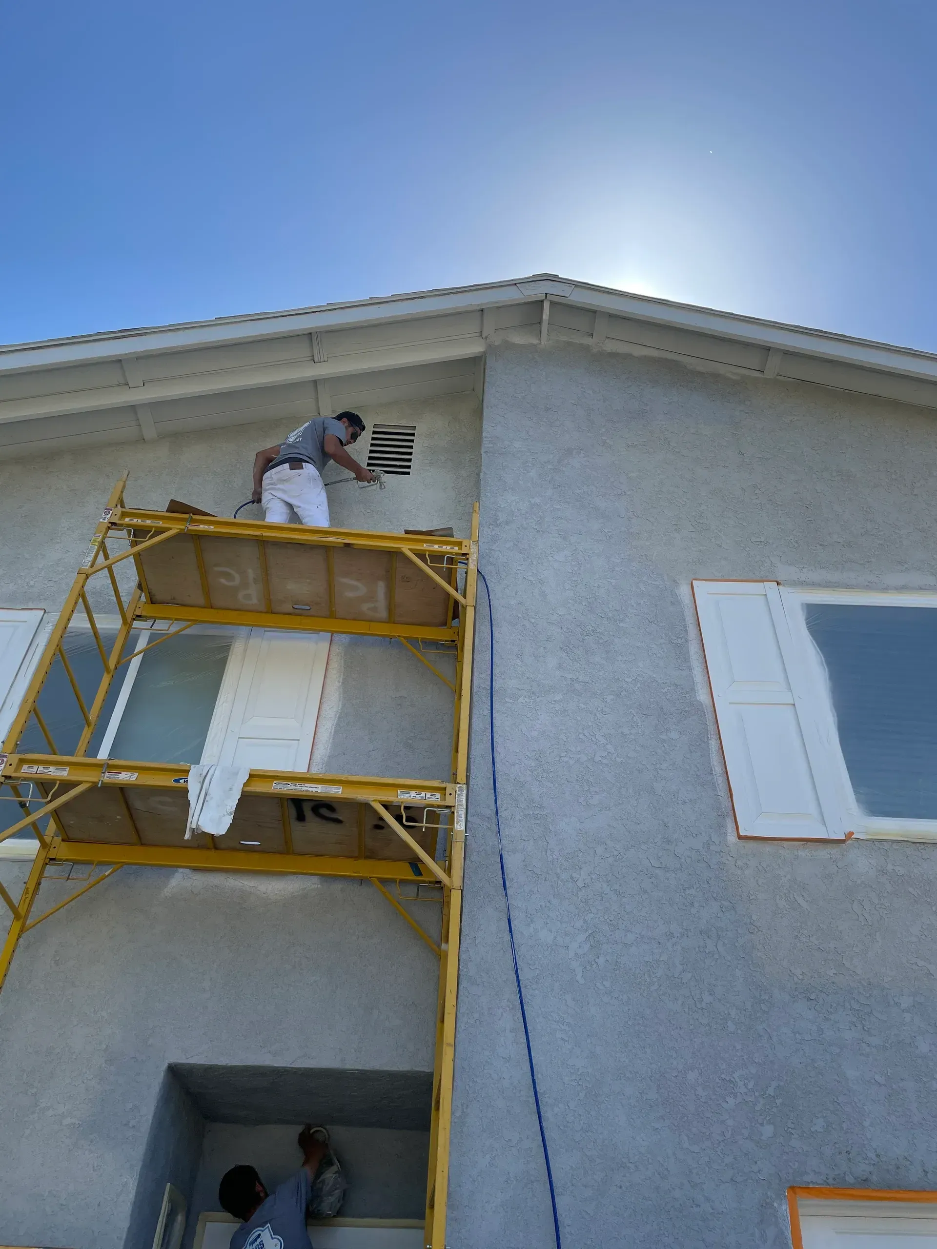 A man is sitting on the floor painting a wall with a roller.