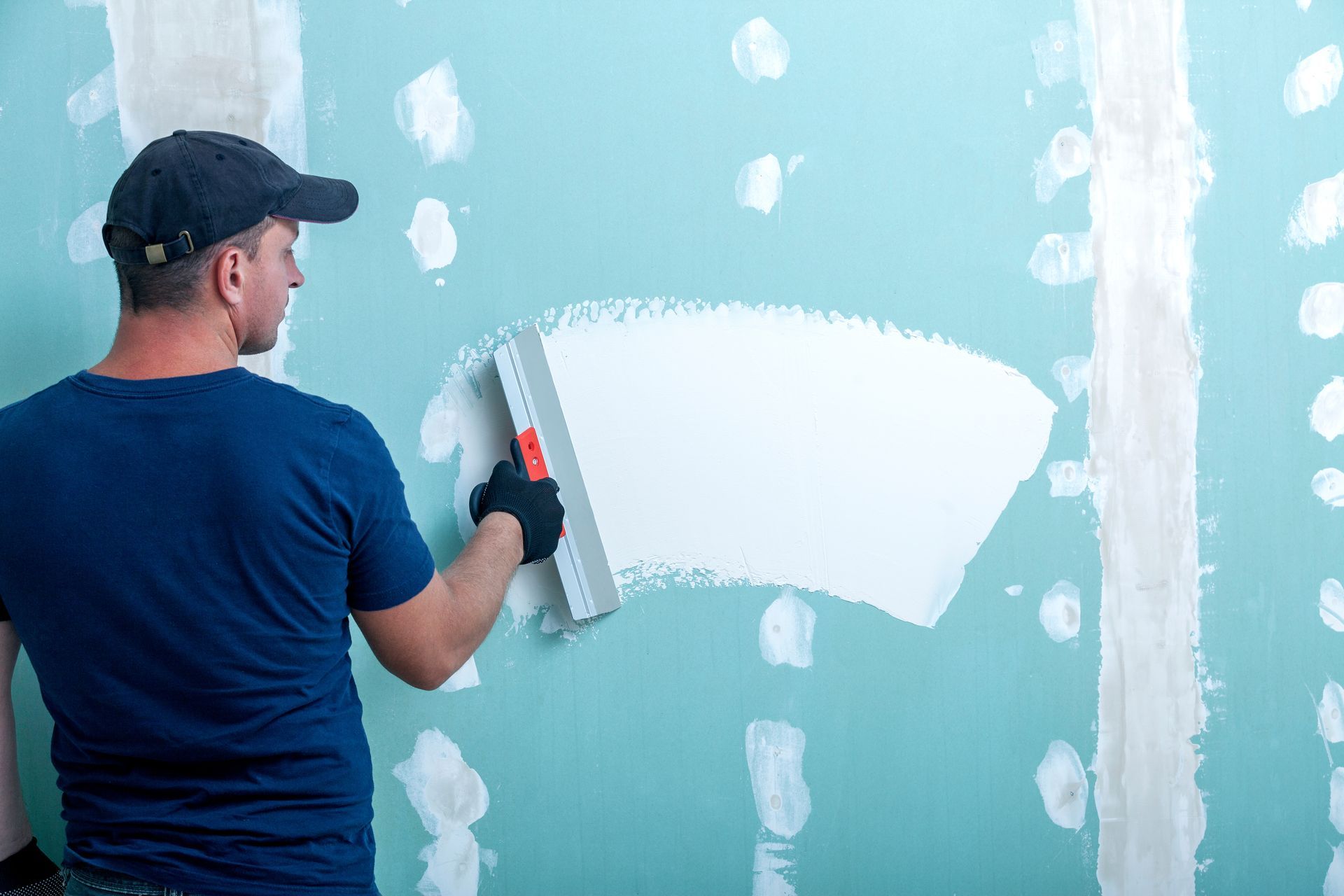 A man is sitting on the floor painting a wall with a roller.