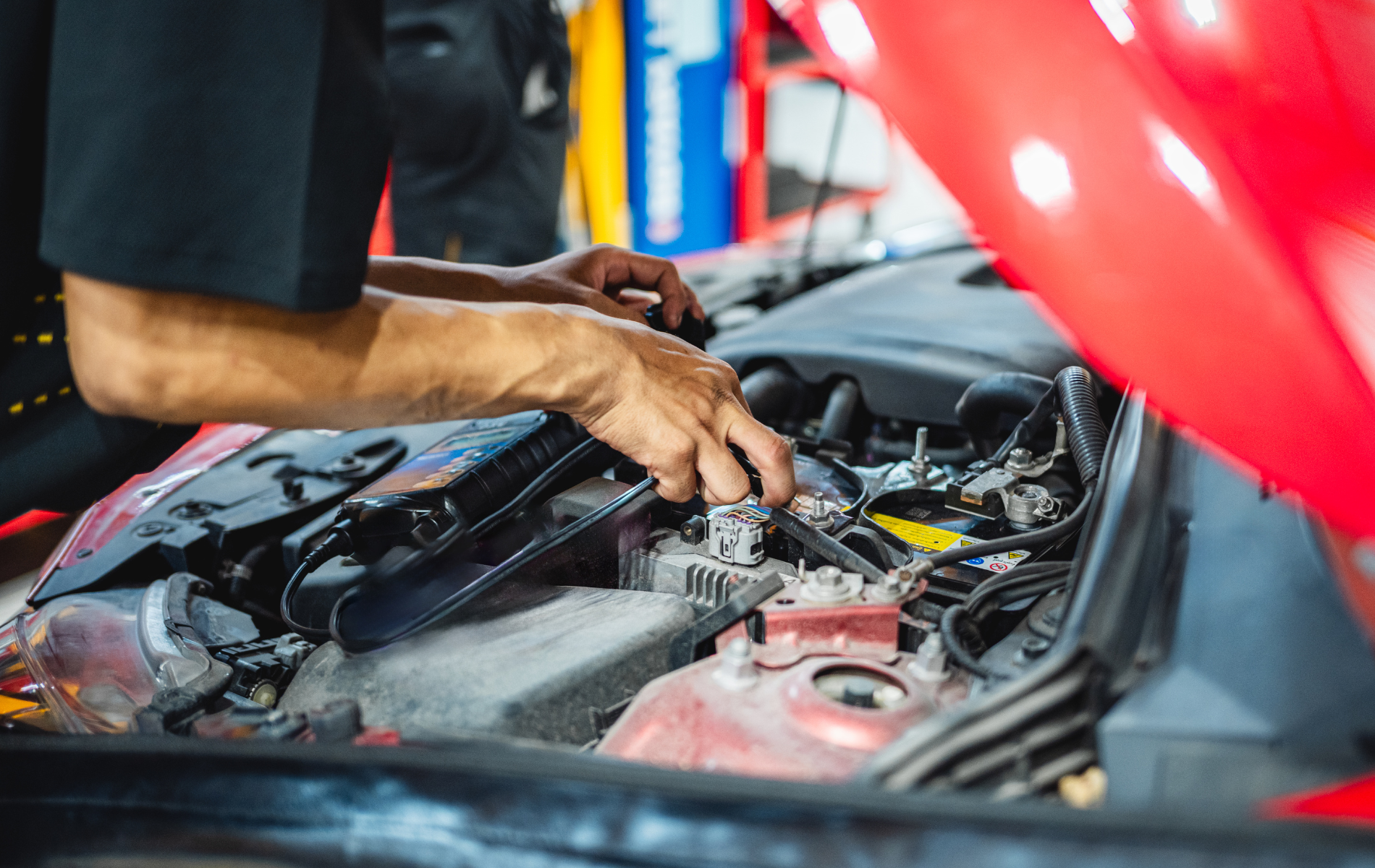 Mechanic working on a red car engine with the hood open.