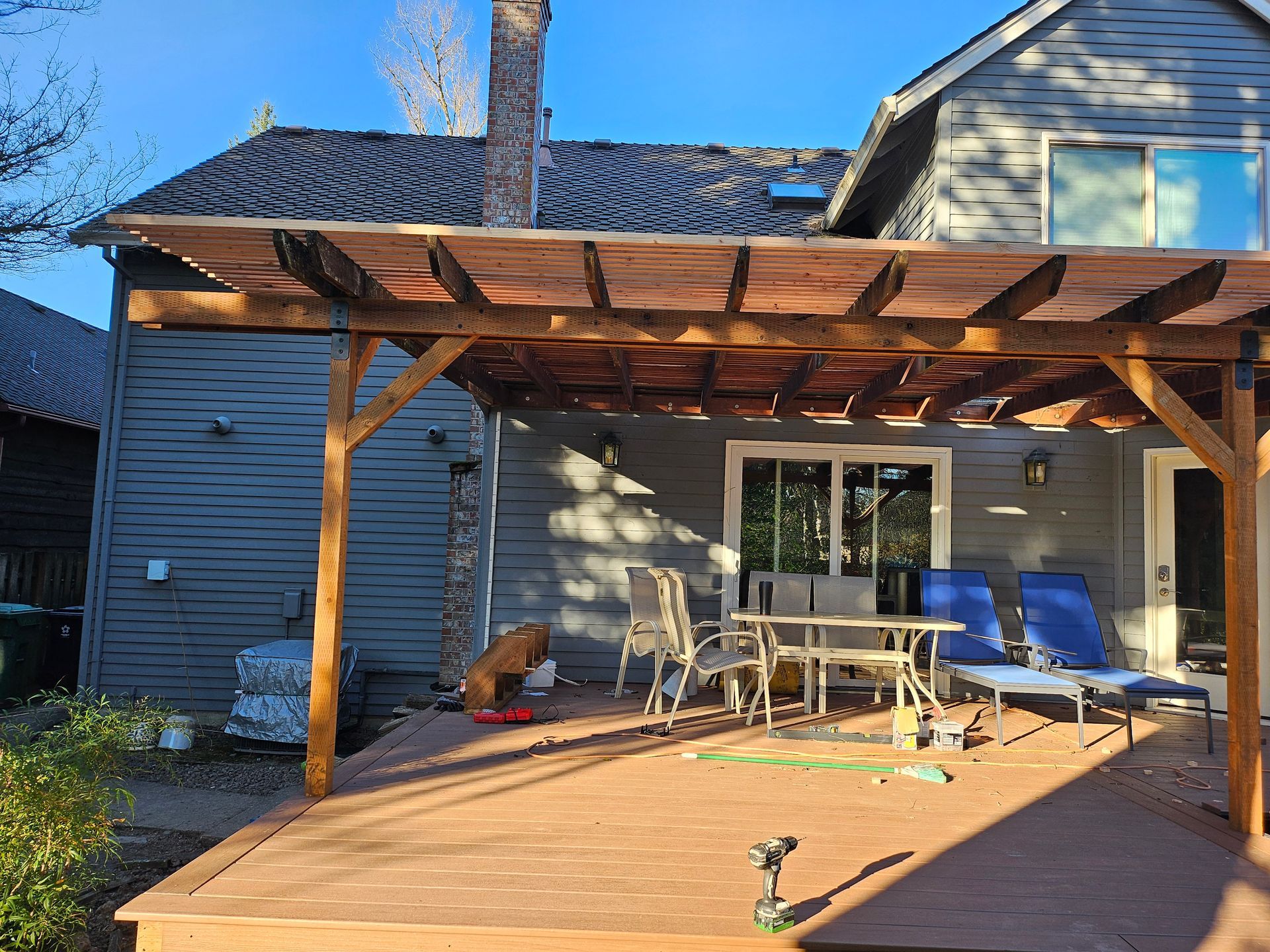 A wooden deck with grey, horizontal planks extending from a sliding glass door against a brown-sided house.