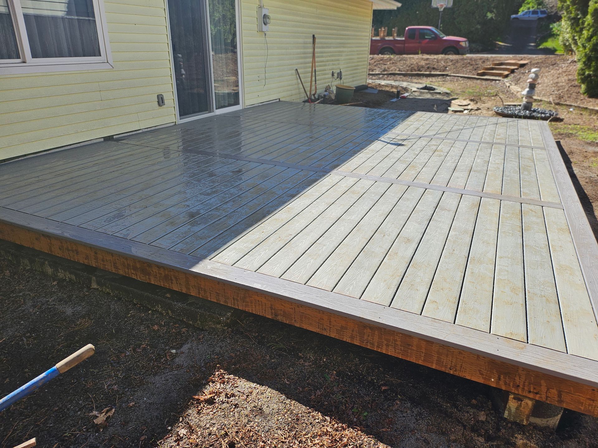 A wide-angle view of a newly installed, wet brown composite deck attached to the back of a grey-sided house.