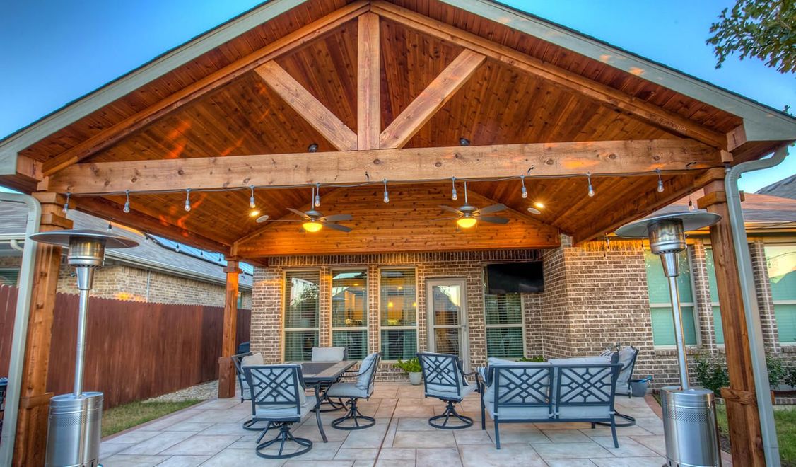 A stone-paved patio faces a building wall made of a rustic stone base, wooden framing, and long, dark-wood lattice windows.