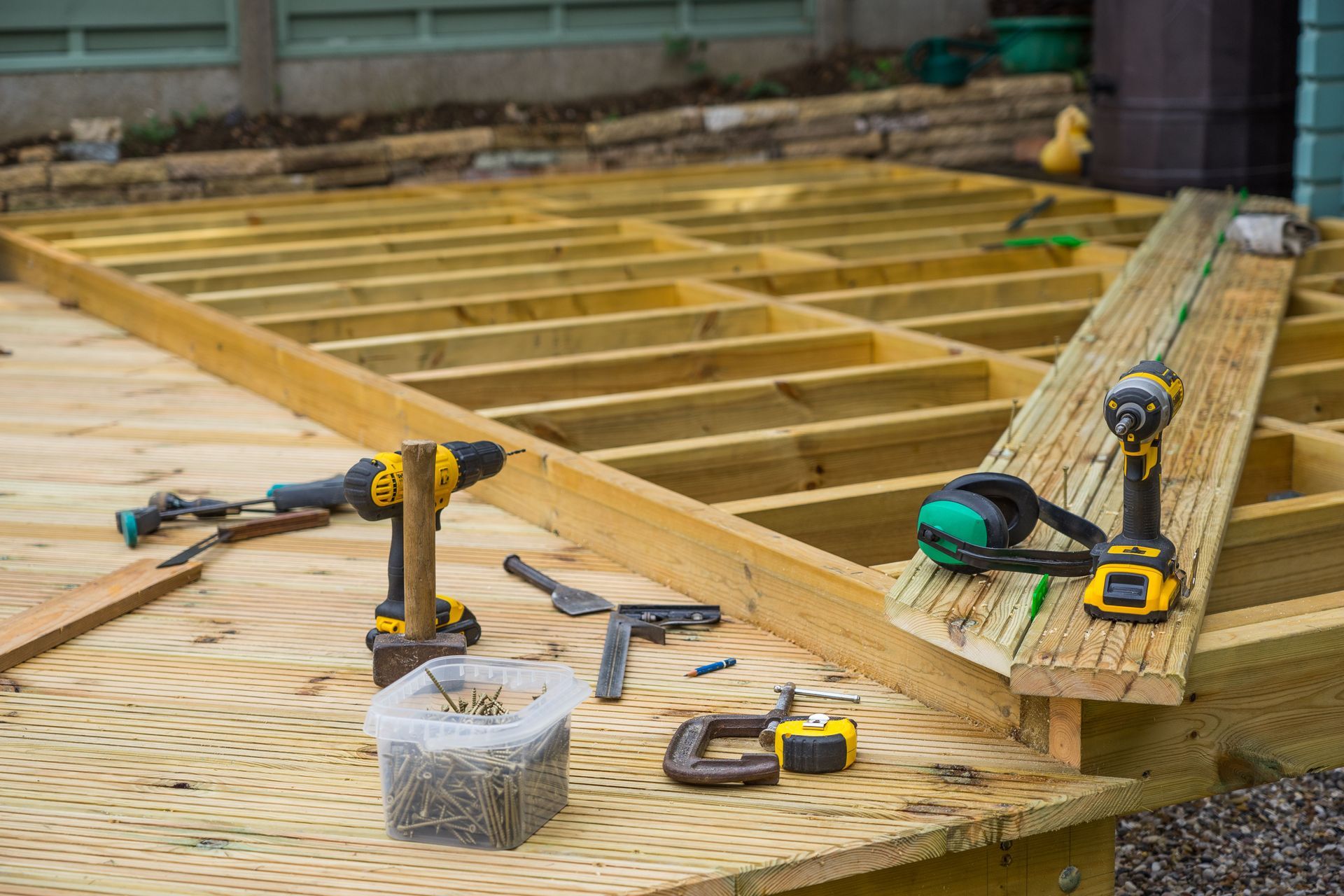 Partially built wooden deck frame with tools, drill, tape measure, and nails on the work surface
