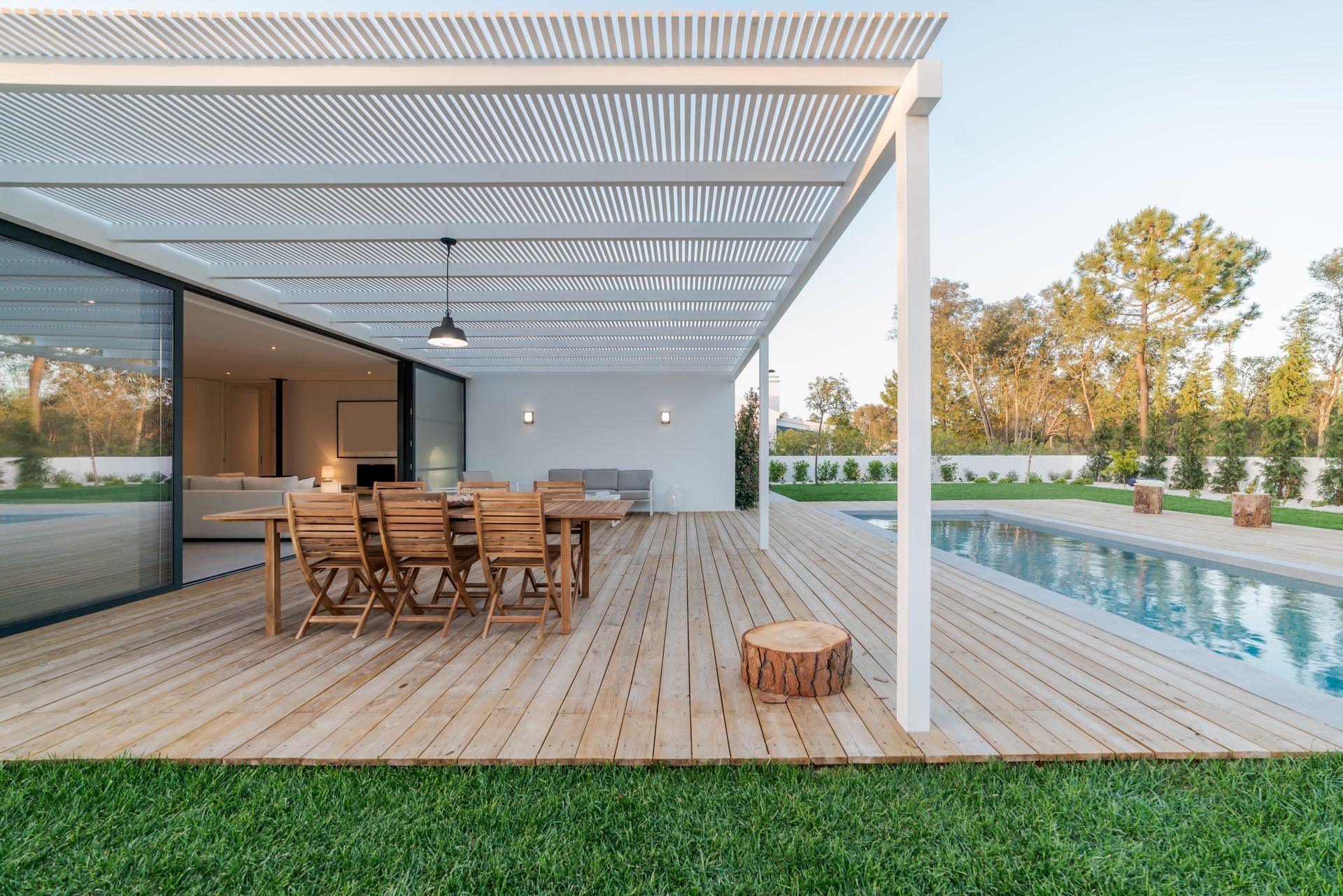 Modern patio with wooden dining table, pergola, and a pool beside a contemporary house