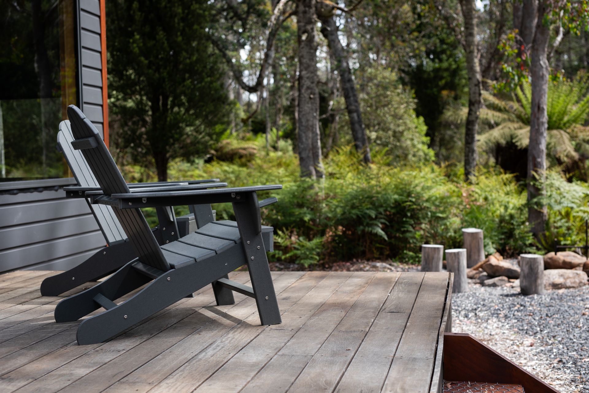 Wooden deck with black lounge chair beside a landscaped garden and trees
