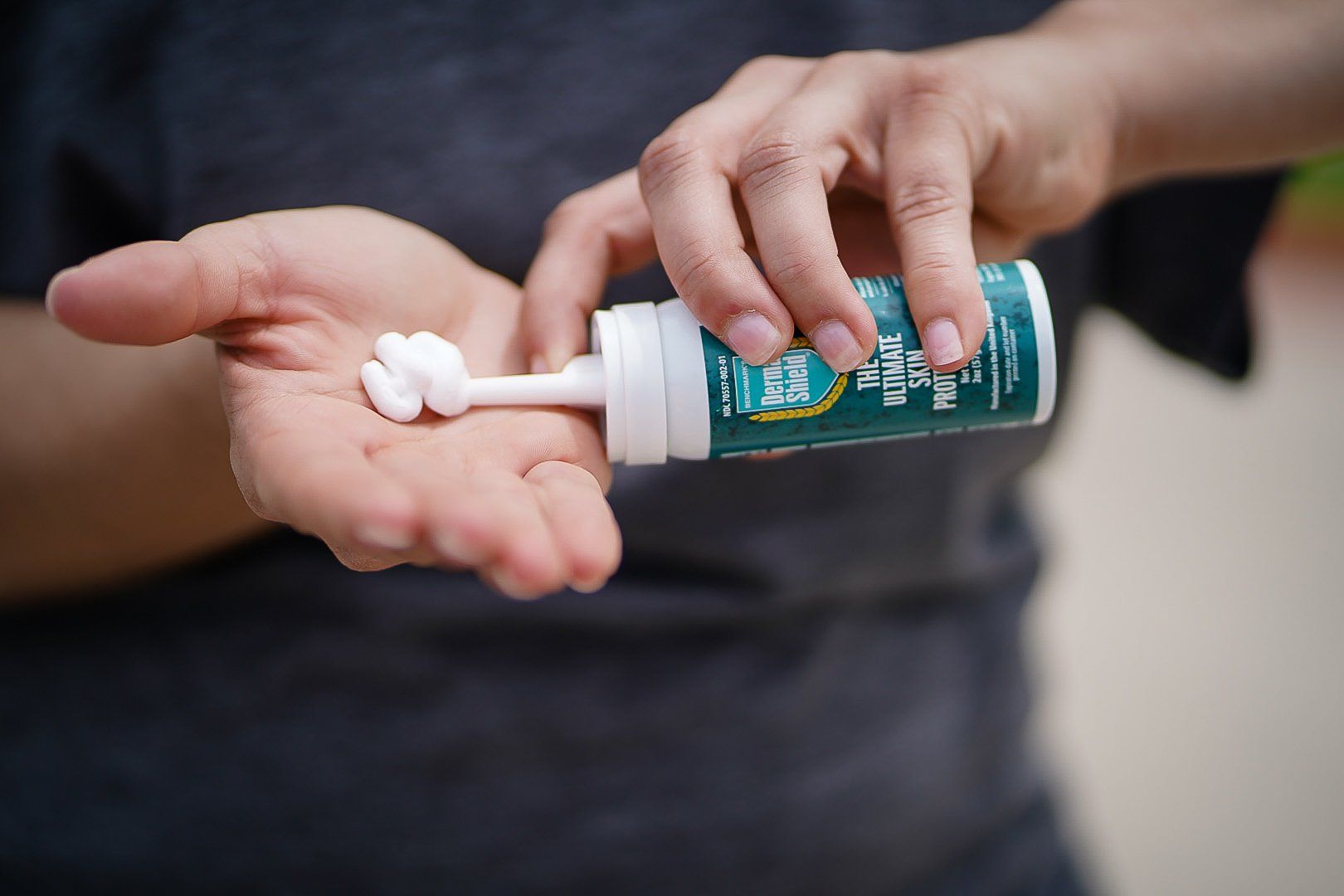 Person dispensing white ointment from a green and white tube into their palm.