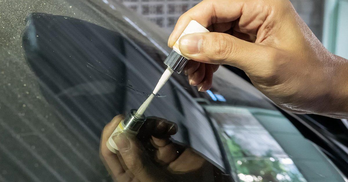 Hand using paint pen to repair a scratch on a black car.