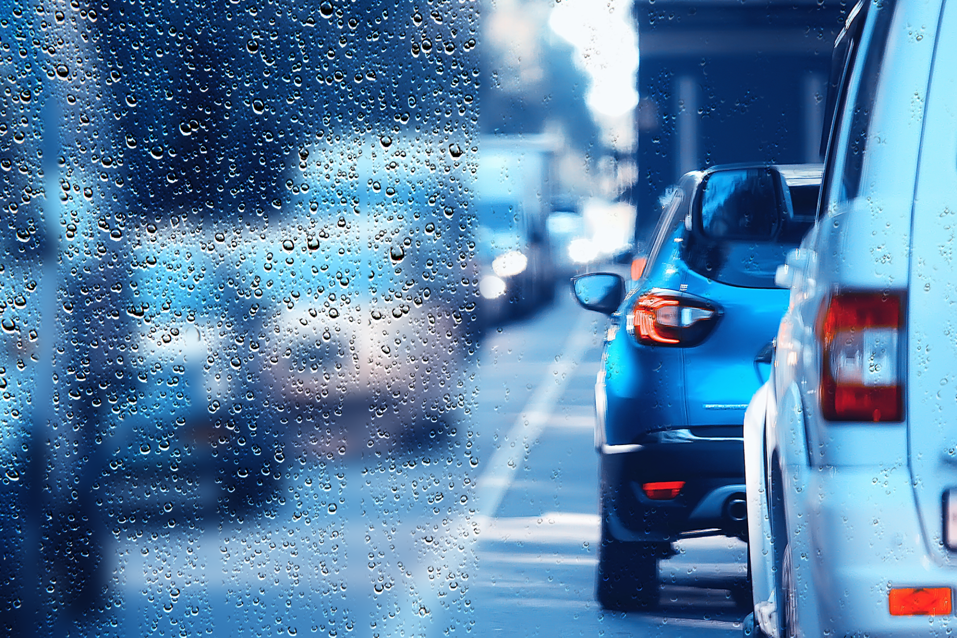 Raindrops on glass with blurred view of cars in traffic.