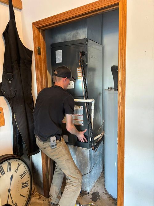 Man installing HVAC unit in a utility closet with a water heater visible.
