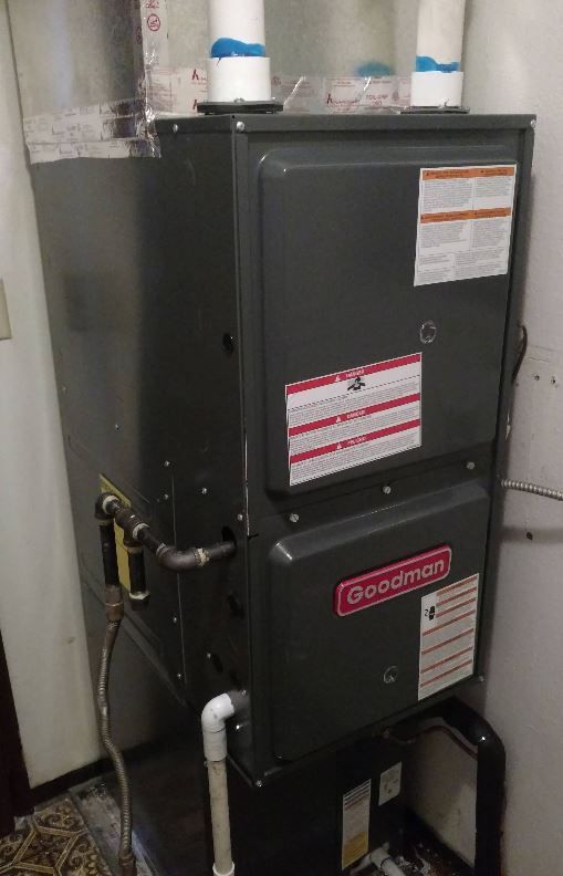 A goodman air conditioner is sitting in a room next to a wall.
