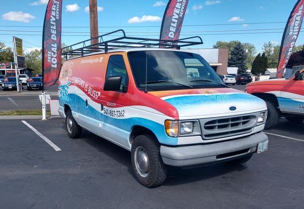 A red , white and blue van is parked in a parking lot.