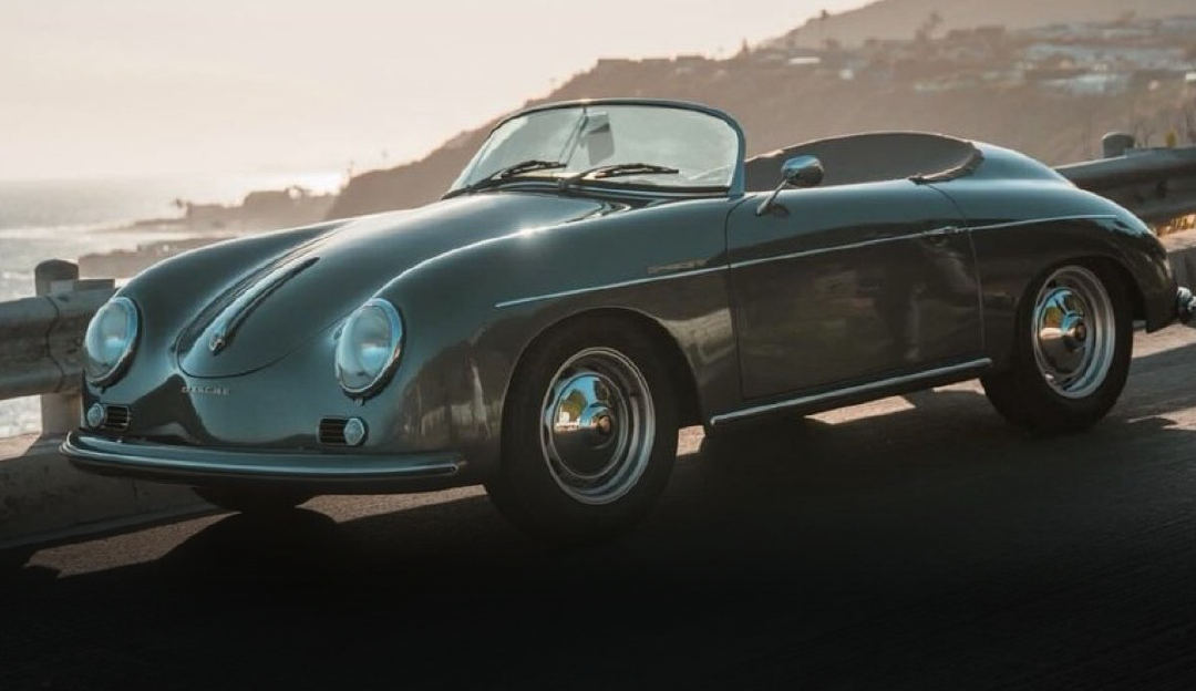 A vintage porsche speedster is parked on the side of the road next to the ocean.
