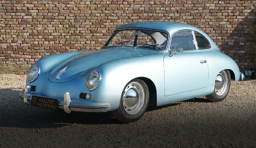 A blue porsche is parked in front of a brick wall.