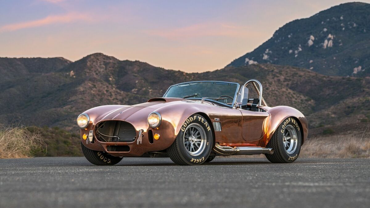 A brown sports car is parked on the side of a road with mountains in the background.