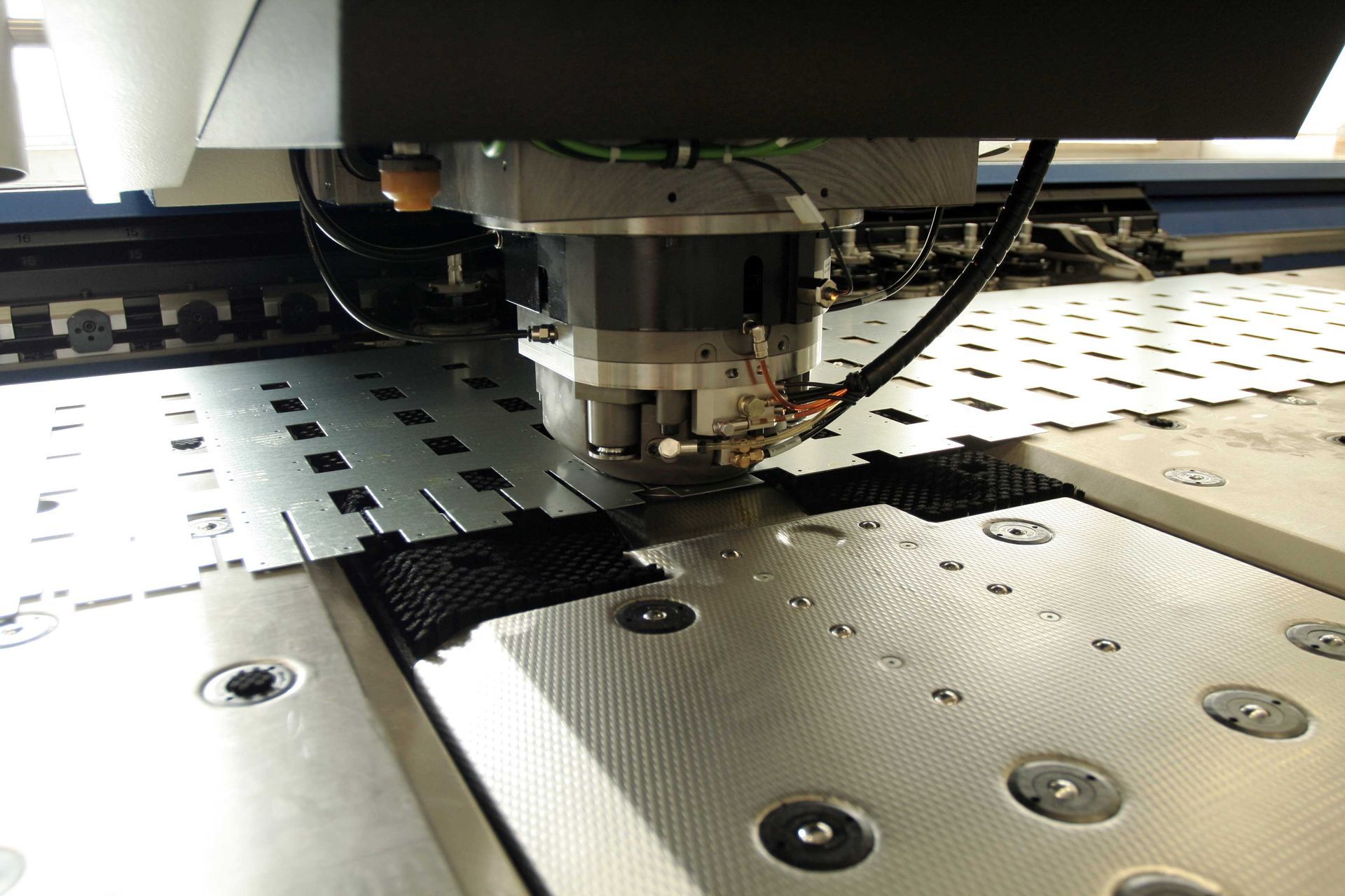 A machine is cutting a piece of metal with holes in it
