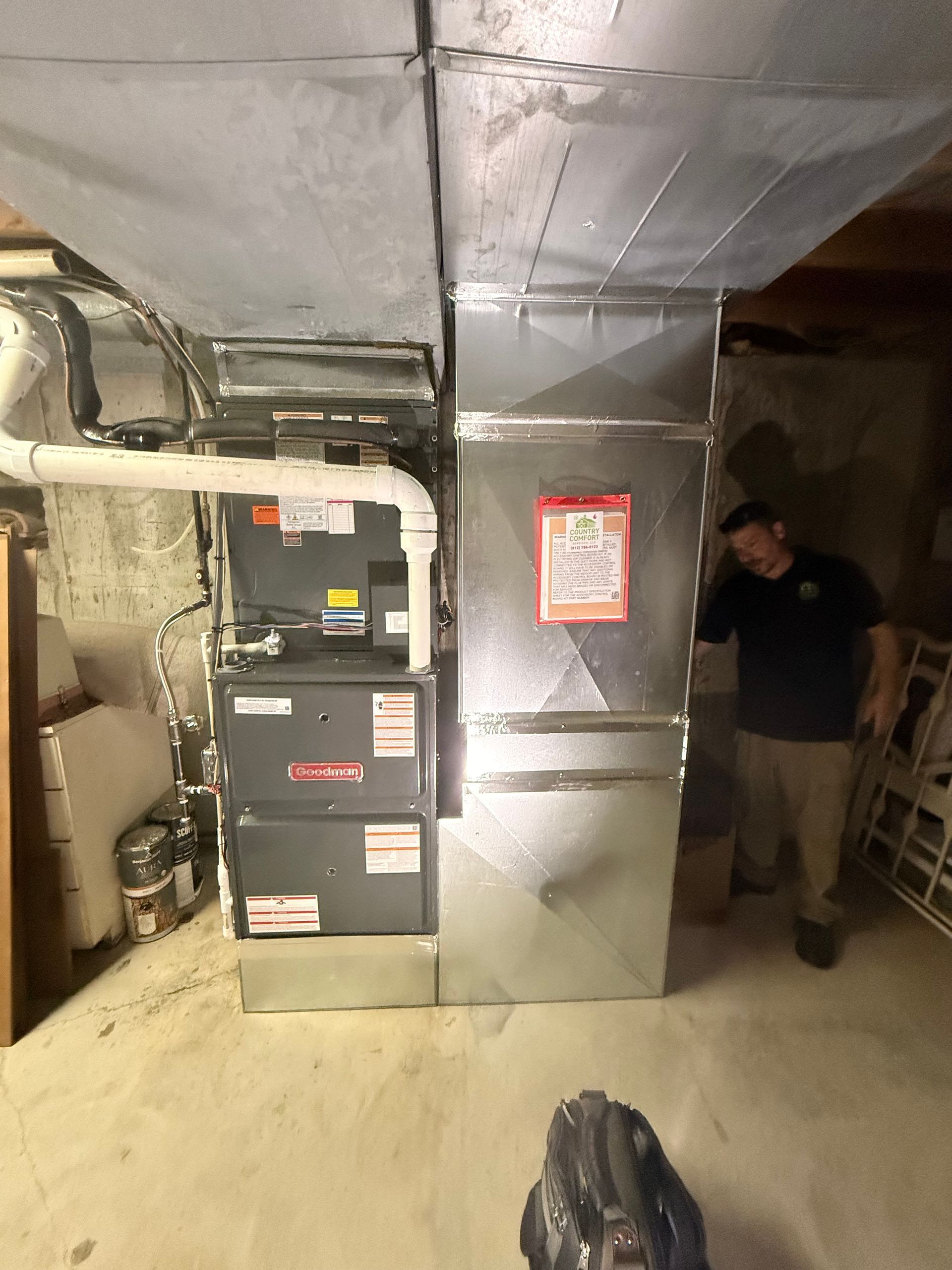 Basement furnace room with HVAC ducts, equipment, and a person standing near the wall.