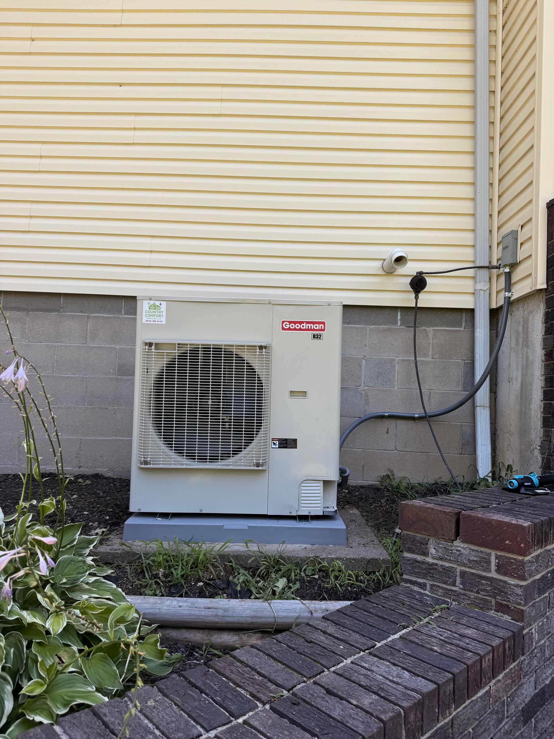 Outdoor air conditioning unit beside a yellow house and brick steps
