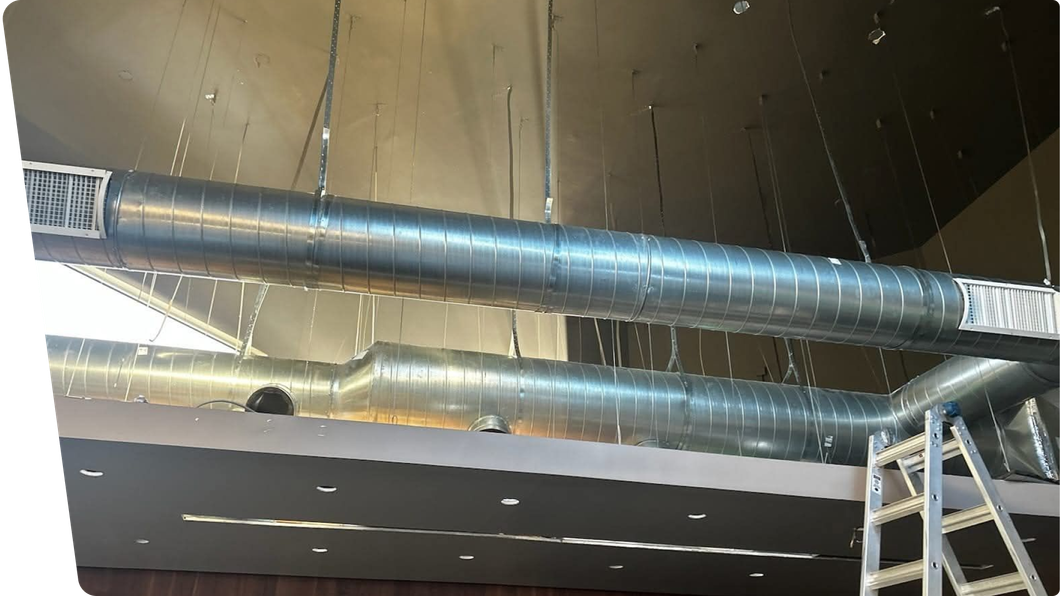 Industrial ceiling with exposed silver ductwork and recessed lights, ladder visible at right.