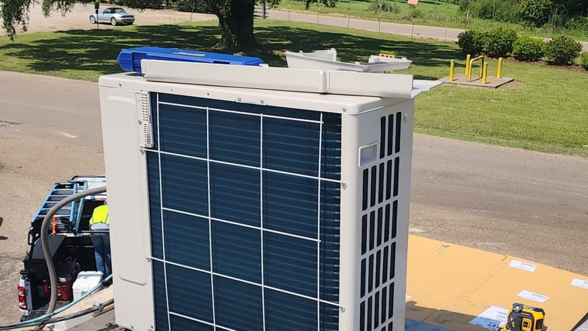 An outdoor HVAC unit sitting on a roof with a technician nearby, during a sunny day.