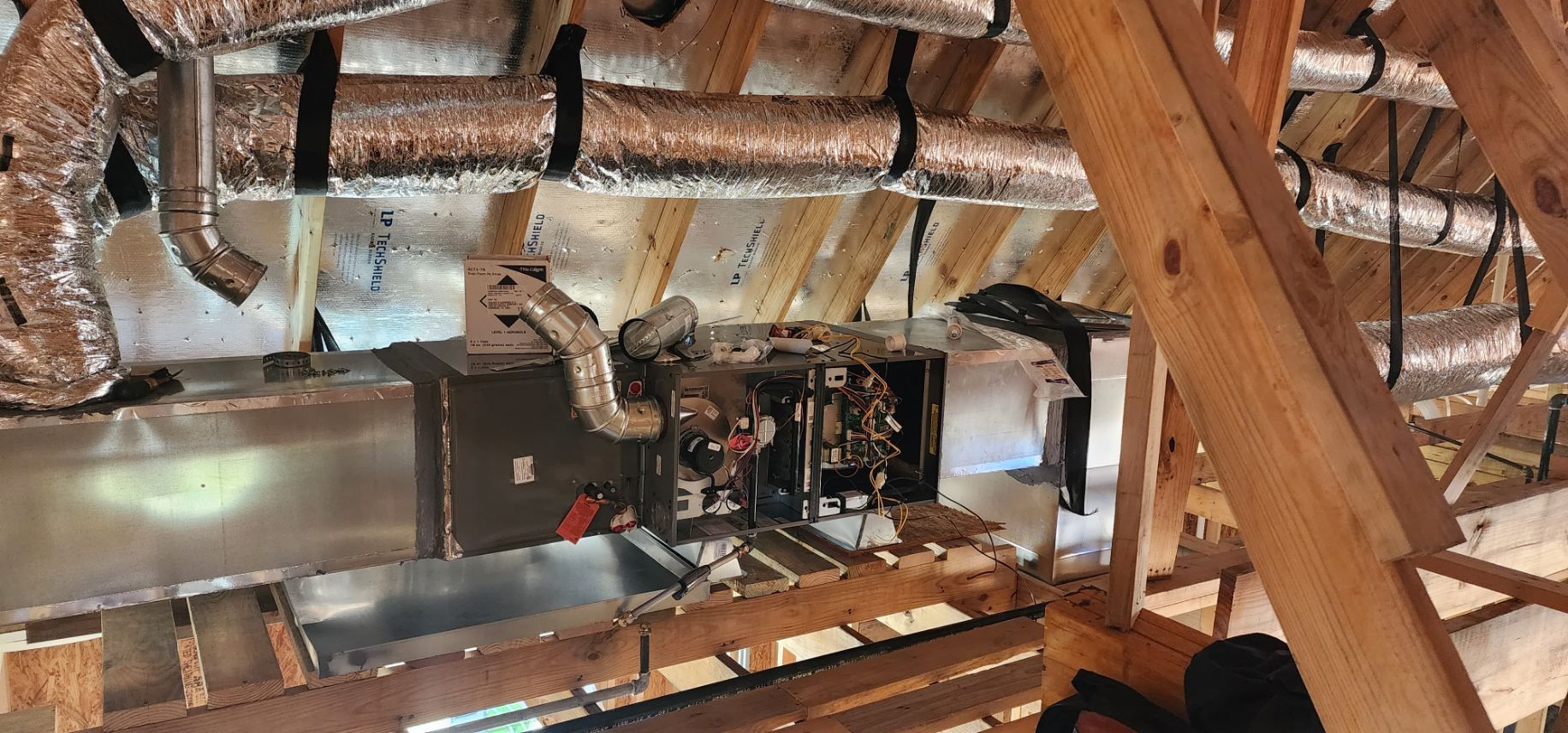 HVAC system in an attic with ductwork, electrical and metal components, wooden beams and framing.