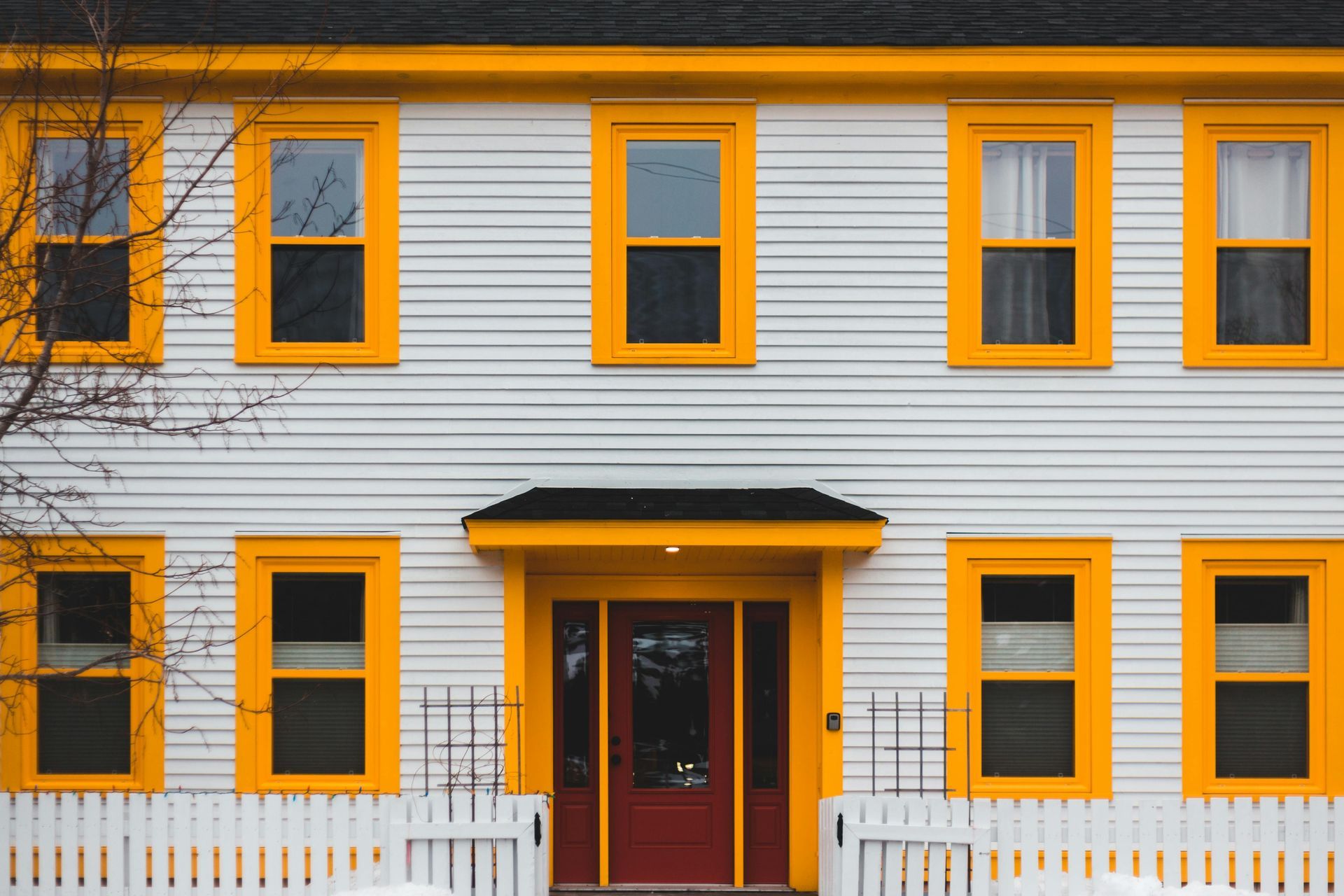 White house facade with bright orange window frames and a red front door behind a white picket fence
