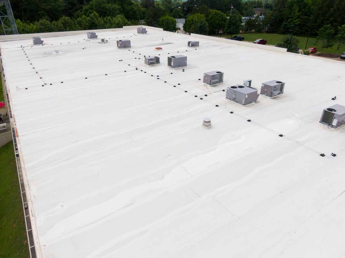 White flat rooftop with several HVAC units surrounded by trees and greenery