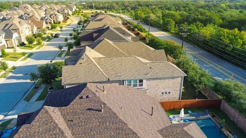Aerial view of suburban houses with brown roofs beside a tree-lined road and green parkland.