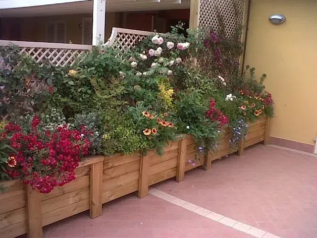 Fioriere in legno piene di fiori colorati accanto al muro del patio di un edificio.