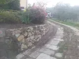 Muro di contenimento in pietra accanto a uno stretto sentiero lastricato, con piante e uno sfondo nebbioso.