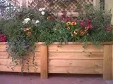 Fioriera in legno piena di fiori colorati e piante verdi in un contesto da giardino.