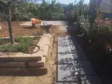 Canale di irrigazione in cemento accanto a un sentiero da giardino con piante e terriccio