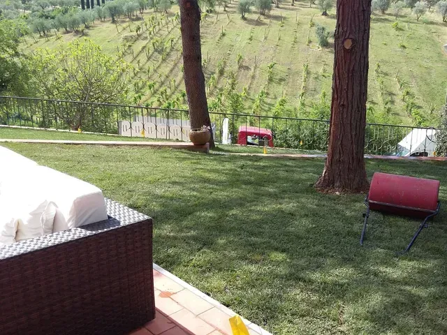 Patio con divano bianco e sedia rossa con vista su un vigneto collinare erboso.